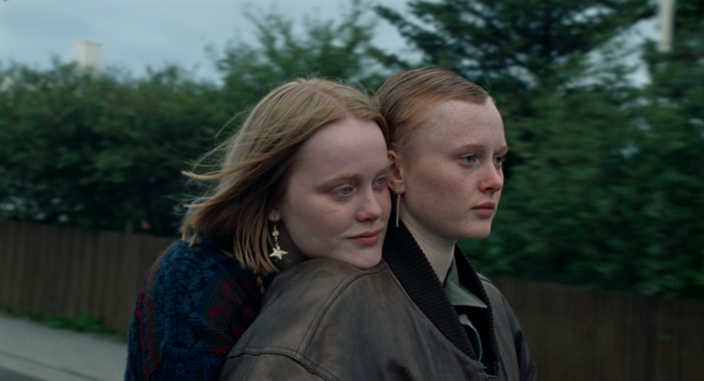 One young woman's head rests on another's shoulder as both stare pensively into the distance, in a screenshot from the Icelandic film When The Light Breaks
